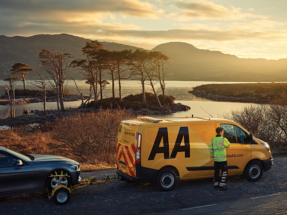 AA recovery van towing a car at side of rural road